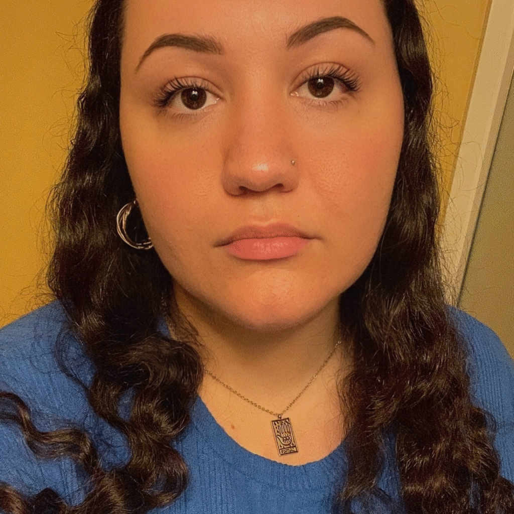 Brenna Thompson looking at the camera. Their long brown hair falls over their blue shirt.