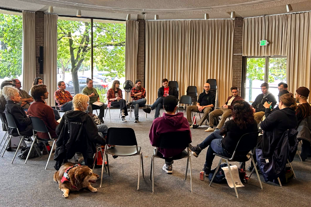 A group of people sitting in a circle in the Santa Rosa Central Library meeting room, a large circular room with trees outside the windows.