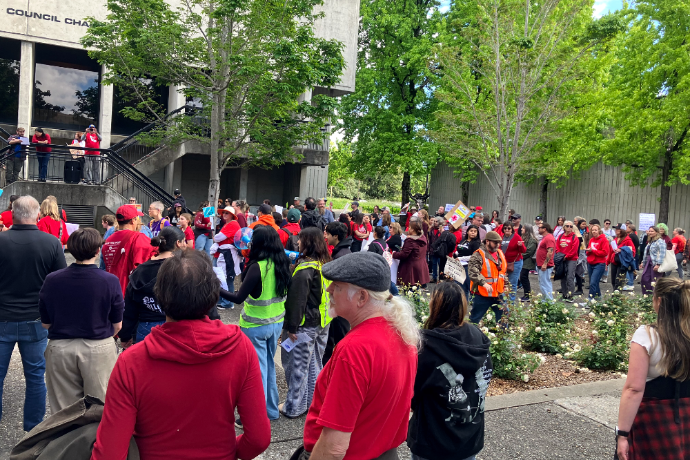 A large crowd of people, most dressed in red, stand outside of Santa Rosa City Hall, spilling out of the entrance.